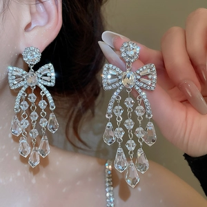 Detailed view of silver bow-knot tassel earrings with sparkling rhinestones and drop gems