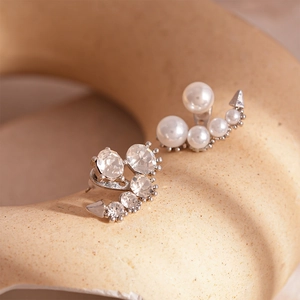 Macro view of silver asymmetric earrings with crystals and imitation pearls on ceramic