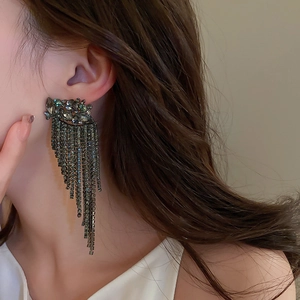 Close-up of elegant long fringe tassel earrings with green rhinestones on model