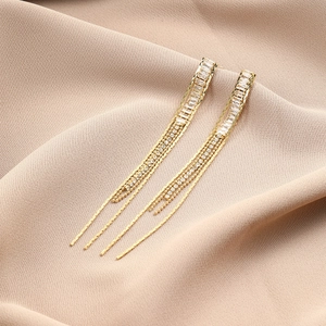 Detail of long gold tassel earrings with rectangular cubic zirconia on silk background