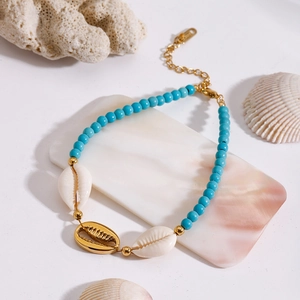 Detail of turquoise bead anklet with natural shells and golden pendant on marble