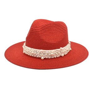 Detail of red straw fedora hat featuring elegant white pearl band and woven texture