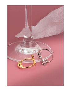 Detail view of gold and silver adjustable spinner rings with rotating beads on a pink surface