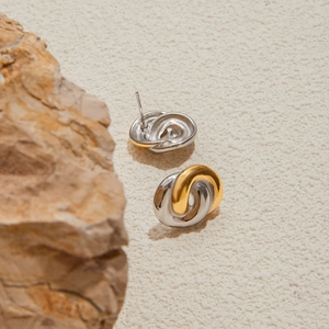 Detailansicht zweifarbiger gedrehter Creolen in Gold und Silber auf einem Stein-Hintergrund