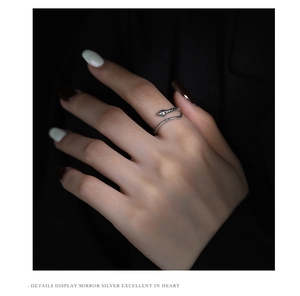 Detail of silver snake ring on hand with green gemstone eyes and textured wrap design