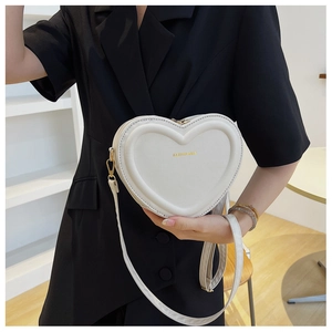 Dettaglio di una borsa a tracolla beige a forma di cuore in pelle PU indossata da modella