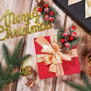 Close-up of a red Christmas gift box with golden ribbon, pine needles, and red berries