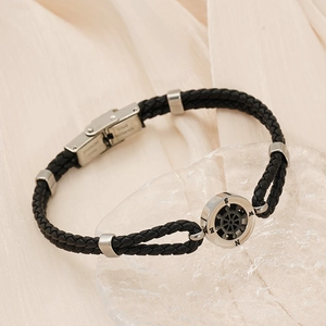 Men's black braided leather bracelet with stainless steel compass charm on silk background