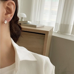 Detail of 925 silver pearl stud and teardrop stone earring set worn in a cozy setting