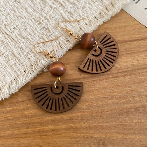 Détail de boucles d'oreilles en bois évidé avec perles marron foncé et crochets dorés