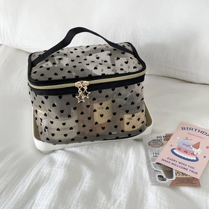 Detail of black heart mesh makeup bag with star zipper and gold hardware on white tray