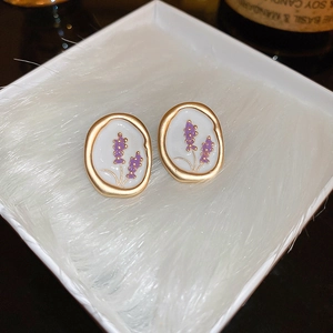Close-up of vintage gold oval earrings with white enamel and purple lavender floral detail
