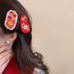 Close-up of red embroidered New Year hair clips with festive greetings and plush edges