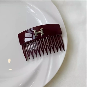 Macro detail of wine red acrylic hair comb featuring a polished silver metal H logo
