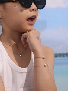 Detail of children's gold chain necklace and bracelets with pearl and green leaf charms