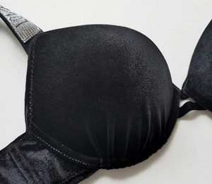 Detail of black velvet bra cup texture and shiny sequined letter shoulder straps