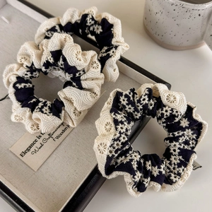 Two black cotton linen hair scrunchies with beige floral lace embroidery on a wooden tray