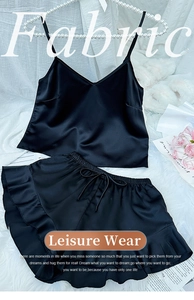 Flat lay of black silk satin pajama set with camisole and ruffled shorts on plush rug