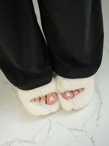 Close-up of white plush faux fur open-toe slippers paired with black lounge pants