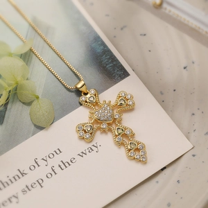 Detailed close-up of a gold cross pendant necklace with green heart gems and zircons