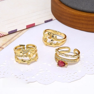 Detailed view of 18K gold butterfly, leaf, and red zircon rings on lace and wood base