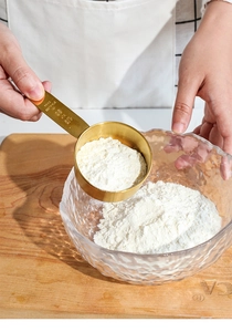 Action shot of 80ml gold stainless steel measuring cup pouring flour into a glass bowl