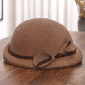 Detail of wool felt beret featuring leaf decor and thin strap on a wooden surface