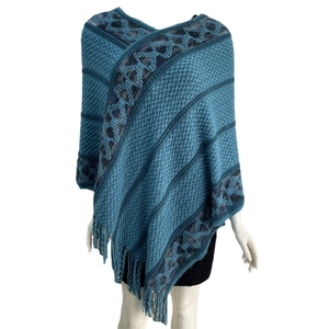 Detailed knit texture of a blue V-neck poncho with geometric patterns and fringe tassels