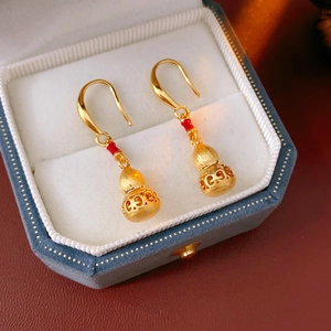 Detailed view of golden gourd-shaped earrings with red accents on a jewelry display