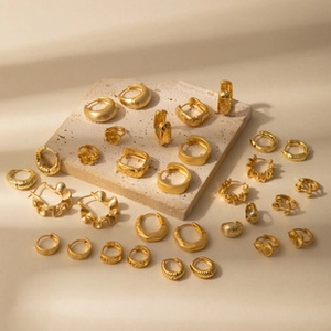 Detailed arrangement of gold earrings and rings on textured stone for jewelry set display