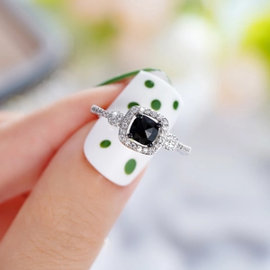 Close-up of a silver ring featuring a square black gemstone with diamond-encrusted border