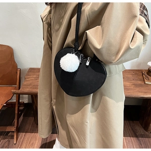 Detail einer schwarzen herzförmigen Umhängetasche aus Matt mit weißem Plüschball-Anhänger