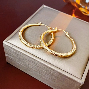 Gros plan de créoles dorées texturées avec détails plissés sur un écrin à bijoux gris