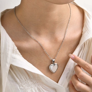 Macro detail of a silver heart locket necklace with white shell inlay worn on a model