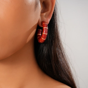 Close-up of red C-shape earrings with gold stripe texture on a model's ear