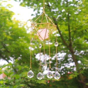 Detail of rose quartz suncatcher with golden geometric frame and hanging crystals