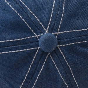 Macro detail of navy denim baseball cap showing contrast stitching and top button
