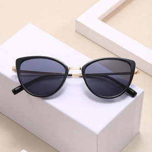 Modern cat-eye sunglasses with black lenses and gold metal bridge on white geometric stand
