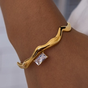 Detail of golden wave cuff bracelet with a rectangular zircon on model's wrist