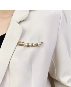 Detail of a gold alloy pearl brooch with rhinestones worn on a white blazer