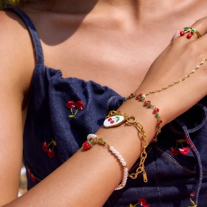 Detail shot of 18K gold strawberry and cherry jewelry set worn on blue denim jacket