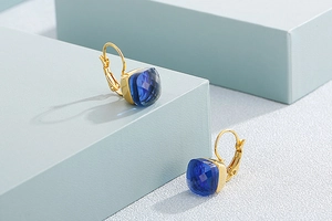 Detailed shot of dark blue square crystal earrings with golden hooks on a blue display