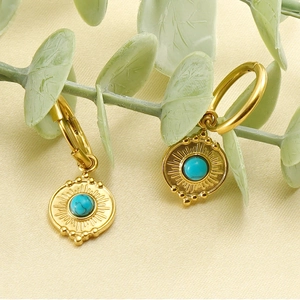 Close-up of golden hoop earrings with turquoise stones and vintage sunburst texture