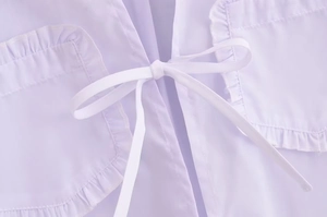 Détail du chemisier lilas avec nœud blanc et poches ornées de volants délicats