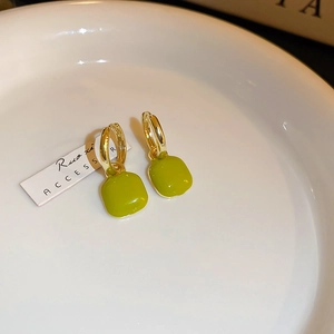 Close-up of green square pendant earrings with golden hoops on a white ceramic plate