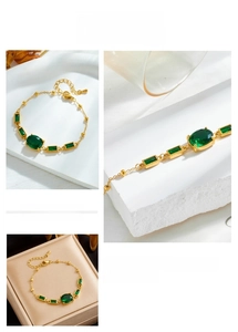 Macro detail of gold-plated chain bracelet with emerald green stones and lobster clasp