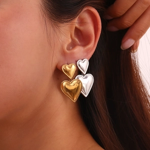 Close-up of two-tone gold and silver heart earrings worn on ear showing stylish scale
