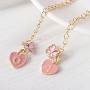Close-up of pink enamel heart and butterfly charms with golden letters on a chain