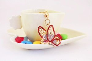 Detail of golden butterfly keychain with red rhinestones and pearls on a tea cup