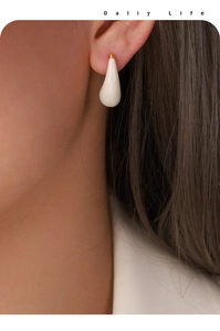 Close-up of model wearing elegant cream enamel teardrop earrings with gold accents